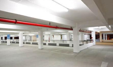 Empty indoor parking garage with white pillars and red pipes overhead.
